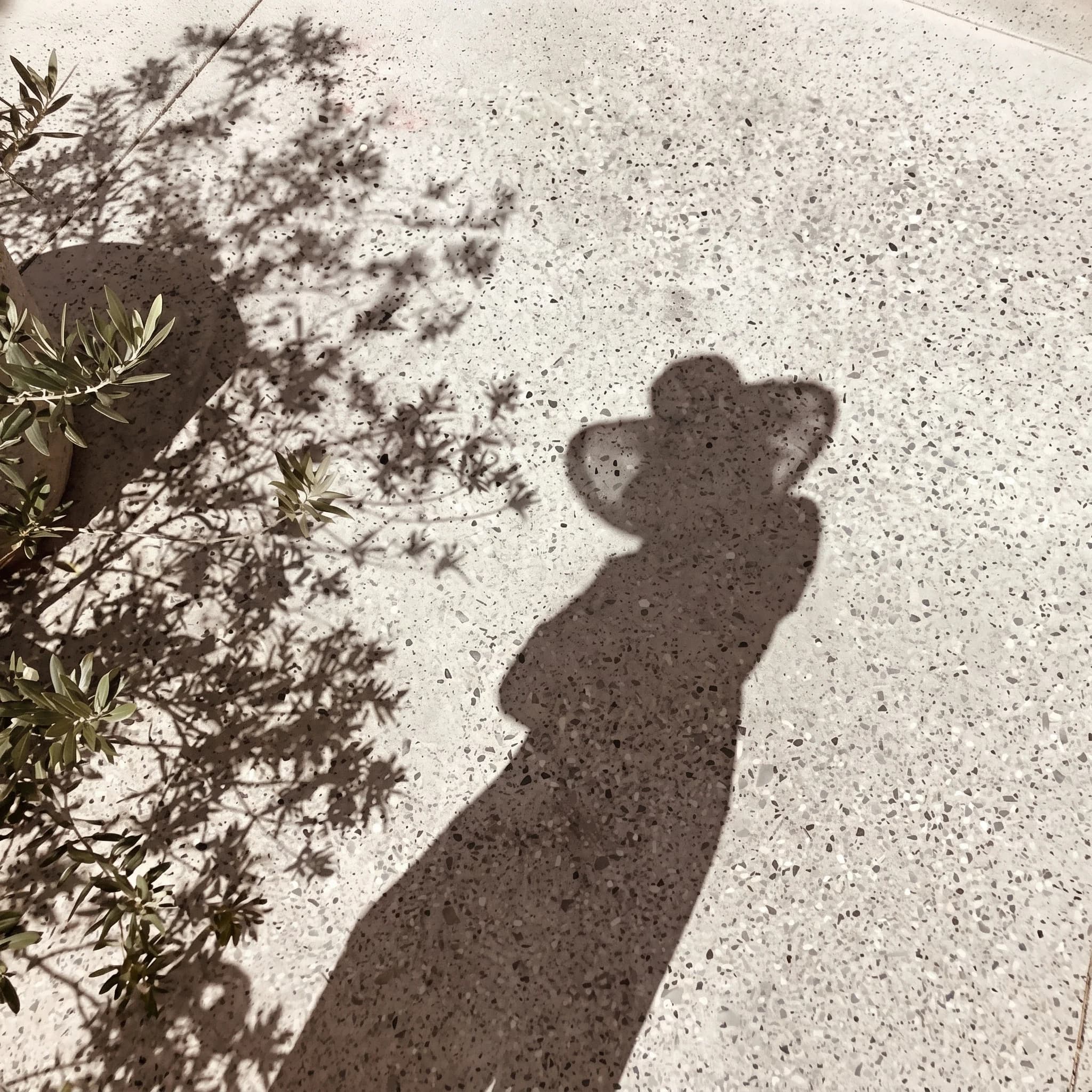Shadow of a person wearing a hat on warm gravel, a quiet moment in sunlight
